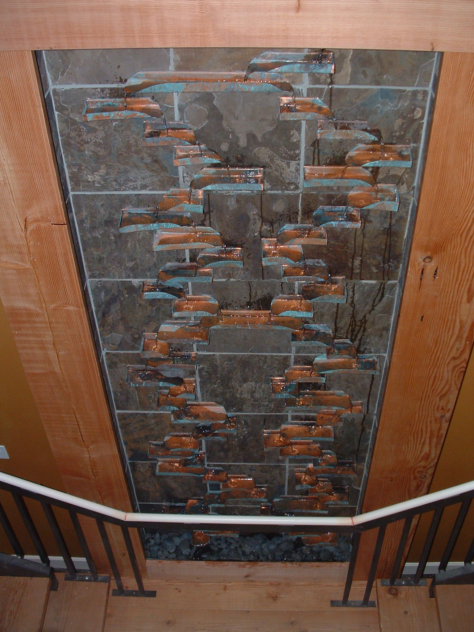 Seattle, WA. Condo for harbor properties, new construction. 4 ft 6 in x 12 ft tall slate backdrop, handmade copper trays with a patina finish, water trickling from pan to pan making its way to the bottom, basin integrated into staircase. 
