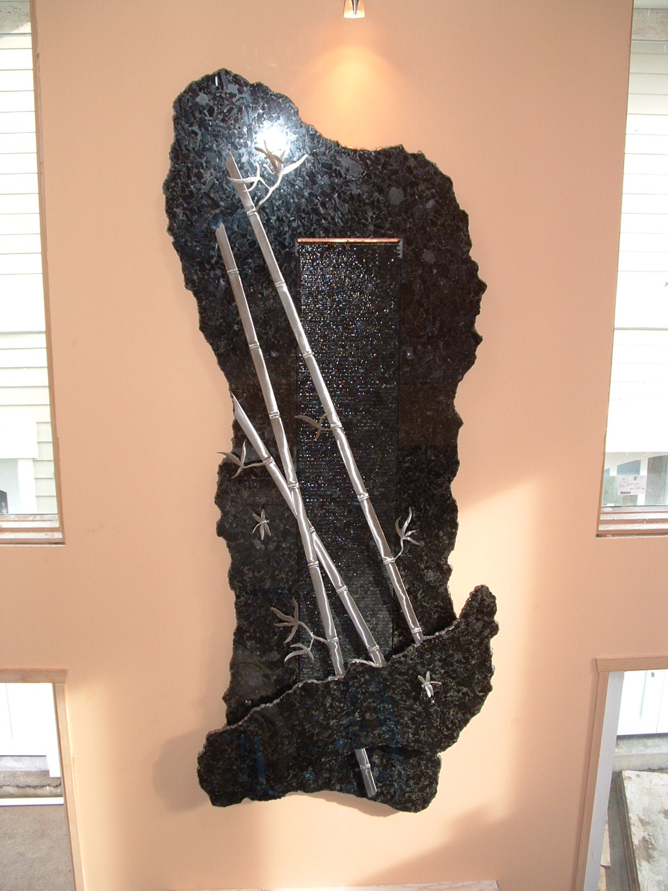 This piece is 4' by 10' tall, made of granite and is mounted on the wall above the fire place 9' off the floor. There is hand made stainless steel bamboo and dragon fly's mounted out in front of the water that is running down the center section wave wall and lighting illuminating from above.
