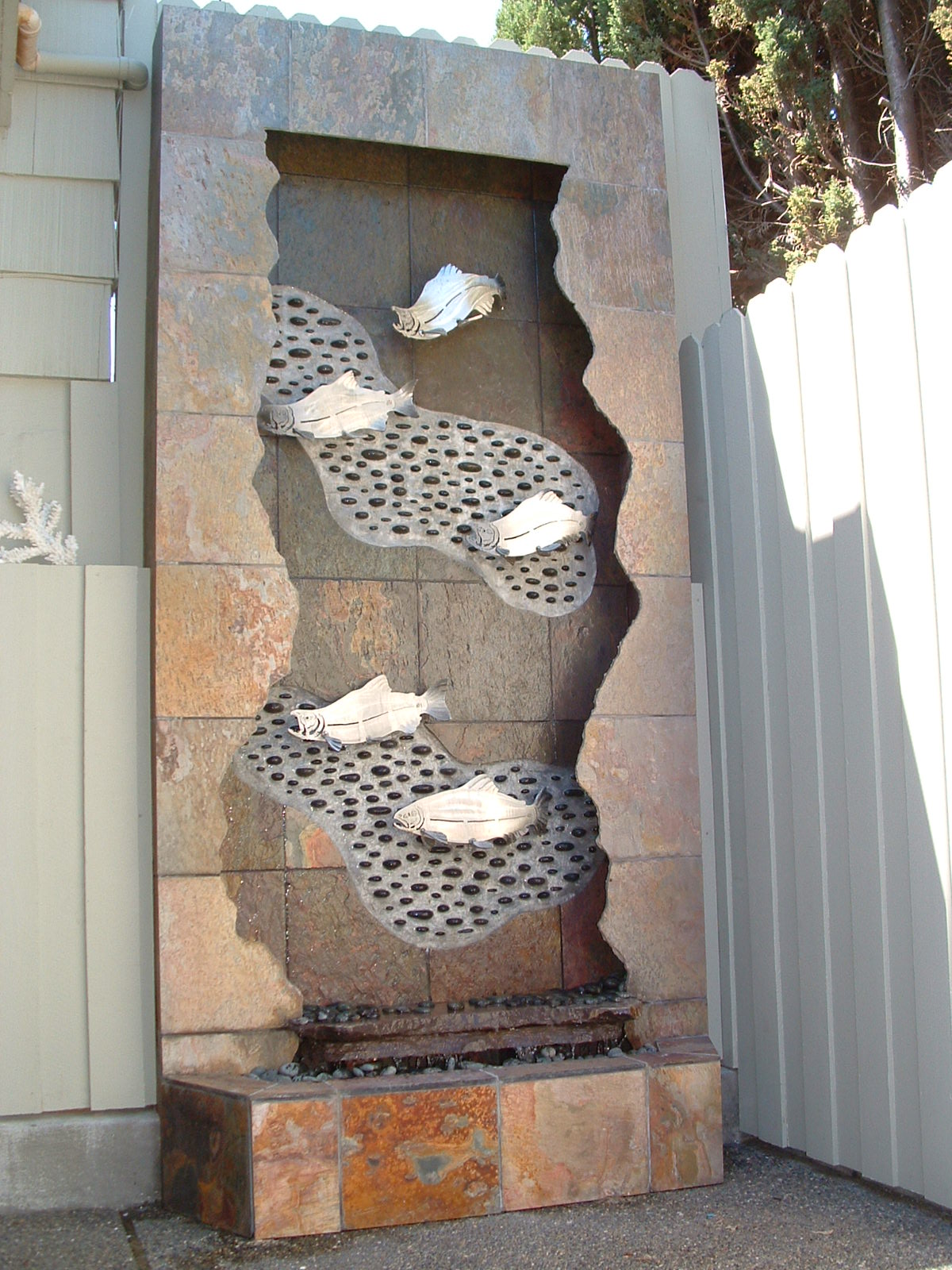 West Seattle, WA. residence, existing home. 5 ft x 12 ft tall, slate, fractured face, inlayed river rock and grouted into place, five 1/4 in. thick stainless steel salmon, two 21/2 in thick slab spillways, auto filler, lighting in valance.